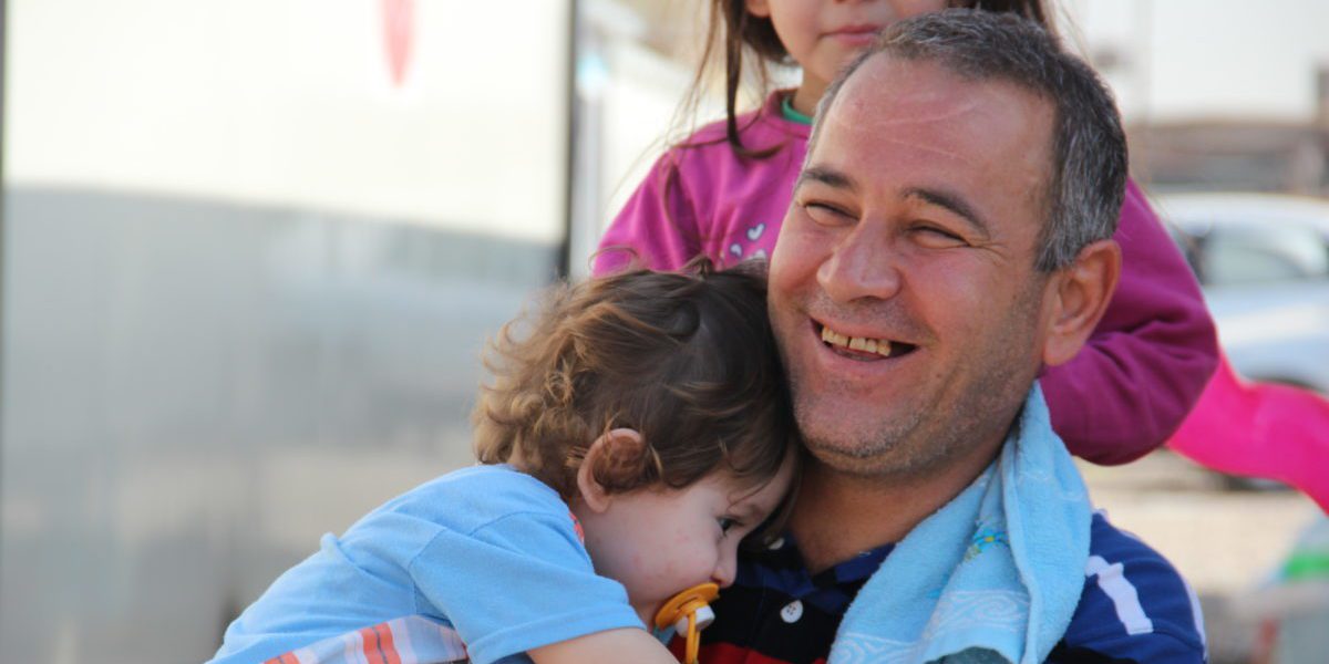Un père iraquien passe quelques temps avec ses enfants hors de sa « maison » dans un quartier informel à Erbit (JRS)